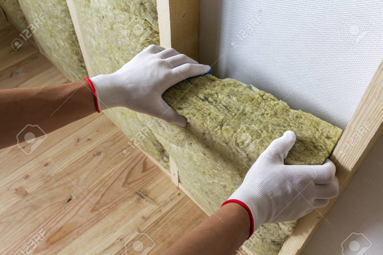 Close-up of worker hands in white gloves insulating rock wool in